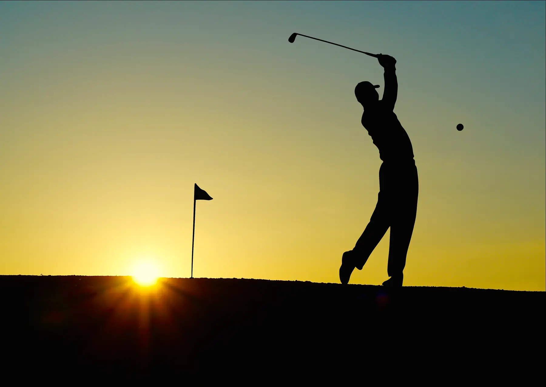 Golfer silhouetted against a sunrise at the top of the follow-through